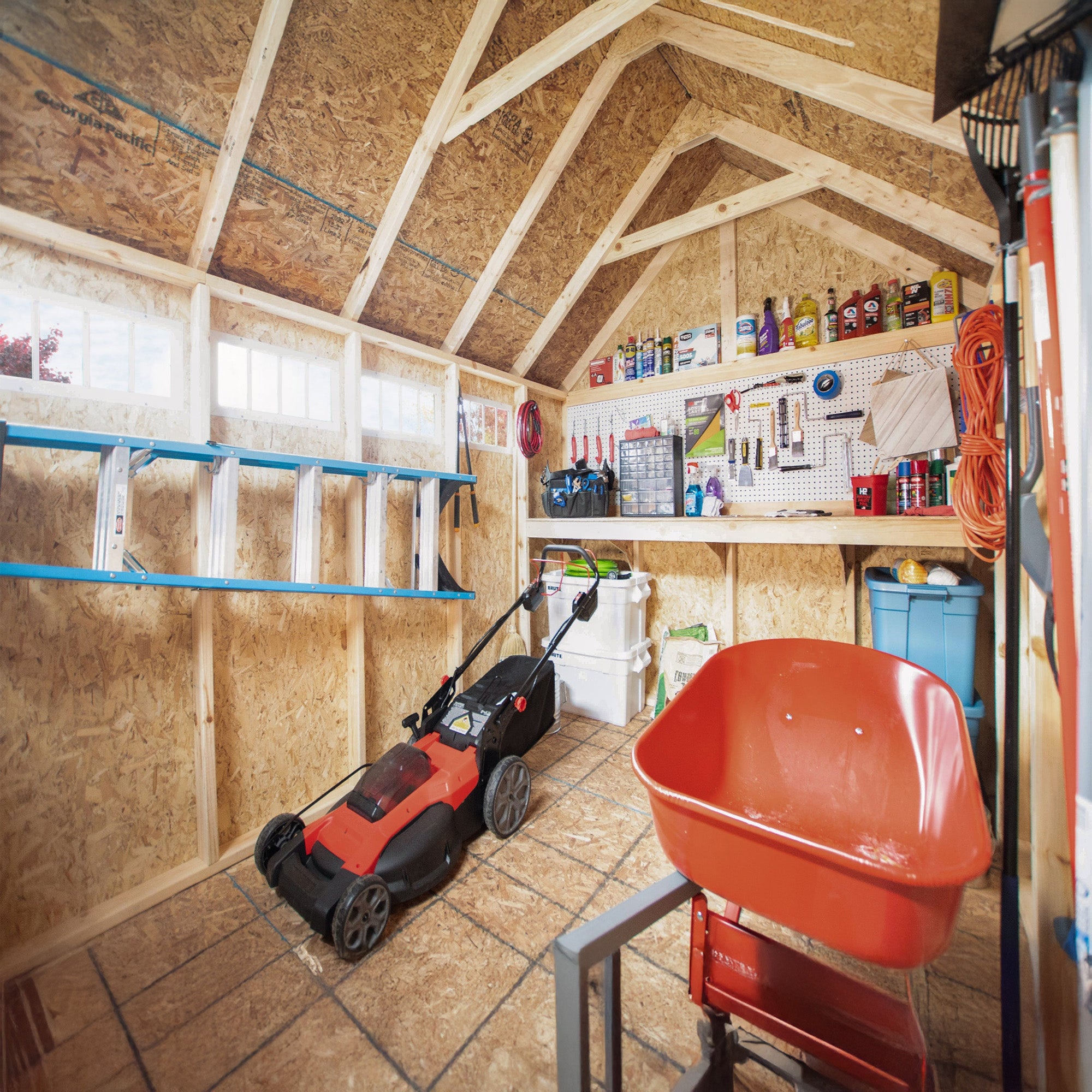 Well-organized shed interior with tools, shelves, a lawn mower, and a wheelbarrow.